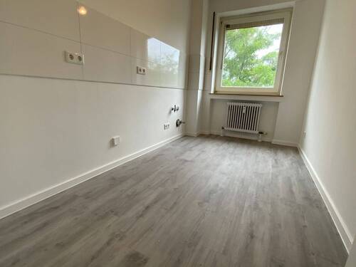 Blick von Diele in Küche mit weißen Fliesenspiegel und weißen Wänden, weißen Fenstern und grauem PVC-Boden - 