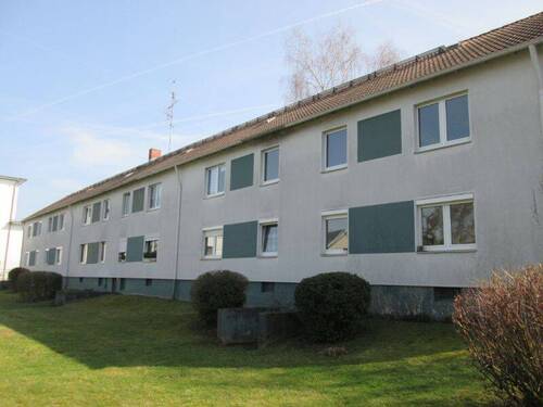 Gebäuderückseite des mehrstöckigen Wohnhauses mit Blick in die Grünanlage mit Sträuchern - 