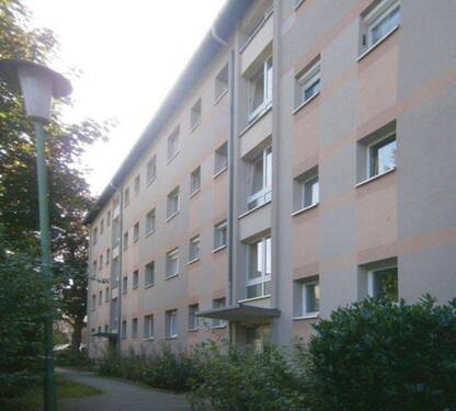 Vorderansicht des mehrstöckigen Wohngebäudes mit Balkonen, umgeben von Grünanlagen mit Bäumen und grünen Sträuchern - 