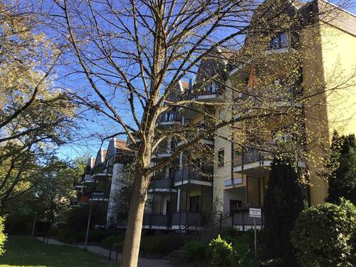 Vorderansicht des mehrstöckigen Wohngebäudes umgeben von Grünanlagen mit Bäumen und Sträuchern - 3-Zimmerwohnung mit 2 Bädern in zentraler Lage kann angemietet werden!