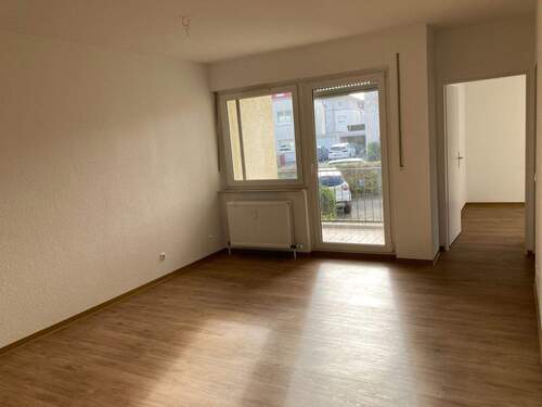 Wohnzimmer mit PVC-Bodenbelag in Holzoptik und Blick zum Balkon und ins Schlafzimmer - 1 Zimmer Etagenwohnung in Friedrichsdorf