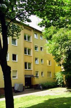 Hausansicht eines mehrstöckigen Wohngebäudes umgeben von Büschen und Bäumen. - 1 Monat mietfrei! 2,5-Zimmer-Wohnung zu vermieten.