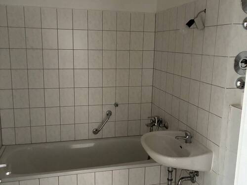 Badezimmer mit Wanne, weißen Sanitärobjekten, weiß-graue Wand- und Bodenfliesen - 