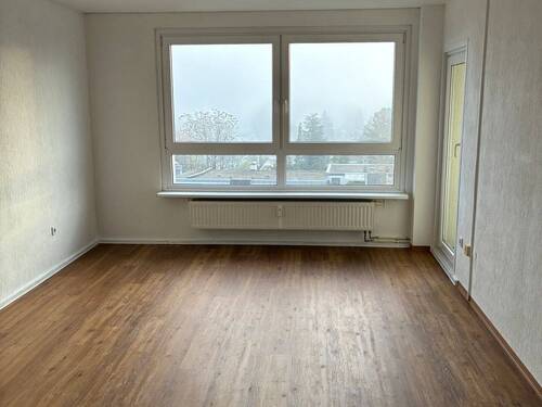 Wohnzimmer mit Zugang zum Balkon, weiß angelegte Wände, brauner Vinyl-Designboden - 