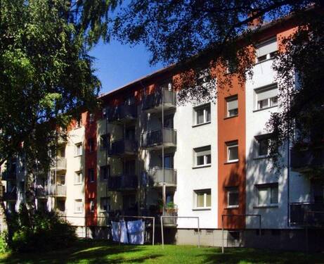 Rückansicht eines mehrstöckigen Wohngebäudes mit Balkonen und umgeben von Bäumen. - Schöne 1-Zimmer-Wohnung sucht Nachmieter!