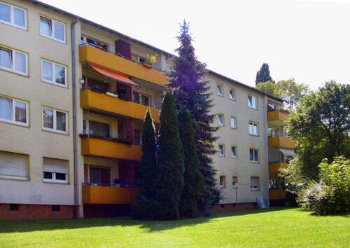 Rückansicht des mehrstöckigen Wohngebäudes mit Balkonen, umgeben von Grünanlagen mit Bäumen und grünen Sträuchern - Toll geschnittene 2 Zimmerwohnung in grüner Wohnlage sucht neue Mieter!