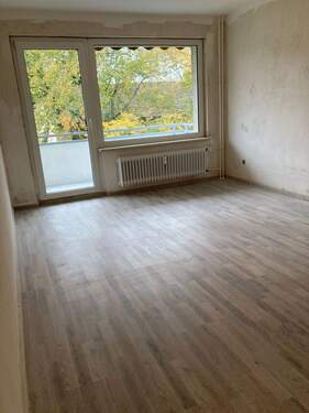 Wohnzimmer mit Bodenbelag in Holzoptik und Zugang zum Balkon - 2 Zimmer Etagenwohnung zur Miete in Frankfurt am Main