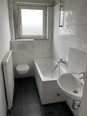 Badezimmer mit weißen Fliesen, Badewanne, Heizung, WC und Waschbecken, Fußboden Antrhrazith - 