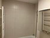 Beige gefliestes Badezimmer mit Badewanne und Wandspiegel - 