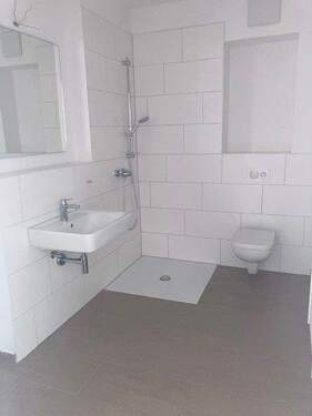 Tageslicht Dusch Badezimmer mit weißem wandhängendem WC, Waschbecken und Handtuch Heizkörper. Die Wände sind im Nassbereich Türhoch und weiß gefliest. Der Boden ist dunkel gefliest. - 1 Zimmer Etagenwohnung zur Miete in Mannheim