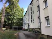 Ein helles Wohnhaus mit Eingang, umgeben von Bäumen und einer Rasenfläche mit Wäscheständern. - Schöne und großzügige 4-Zimmer-Wohnung mit Gäste-WC sucht Nachmieter!