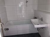 Bad mit Badewanne, weißen Bodenfliesen, dunkelgrauen Bodenfliesen und Waschmaschinenanschluss - 