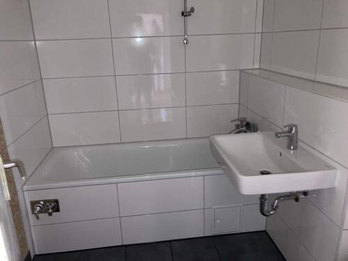 Bad mit Badewanne, weißen Bodenfliesen, dunkelgrauen Bodenfliesen und Waschmaschinenanschluss - 