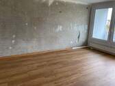 Wohnzimmer mit untapezierten Wänden und braunem Vinylboden in Holzoptik - 