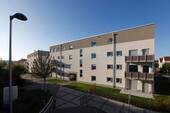 Rückansicht eines mehrstöckigen Wohngebäudes mit Balkonen, umgeben von grünen Rasenfläche und grünen Sträuchern - moderne 2-Zimmer-Wohnung in Raunheim barrierearm