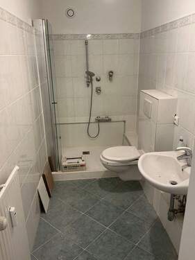 Badezimmer mit weißen Sanitärobjekten und weißen Wandfliesen - 1 Zimmer Etagenwohnung in Wiesbaden