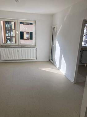Wohnzimmer mit weiß angelegten Wänden, Zugang zum Balkon und Kinderzimmer, heller Linoleumboden - 
