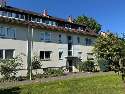 Gebäude Vorderseite des mehrstöckigen Wohnhauses umgeben von Grünanlagen mit Bäumen und Sträuchern - Kleine Wohnung mit gemütlicher Wohnküche sucht neue Mieter!