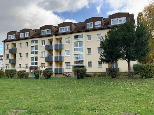 Gebäude Vorderseite des mehrstöckigen Wohnhauses umgeben von Grünanlagen mit Bäumen und Sträuchern - Nachmieter für kleine Familienwohnung in grüner, ruhiger Lage gesucht!