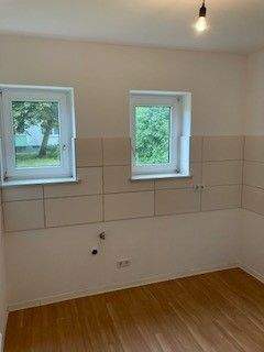 Blick von Wohnzimmer in Küche mit weißen Fliesenspiegel und weißen Wänden, zwei weißen Fenstern und braunem PVC-Boden - 3 Zimmer Etagenwohnung in Meerbusch