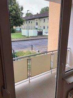 Blick von Wohnzimmer auf Balkon mit grauem Betonboden und Blick auf Rasen der Außenanlage - 