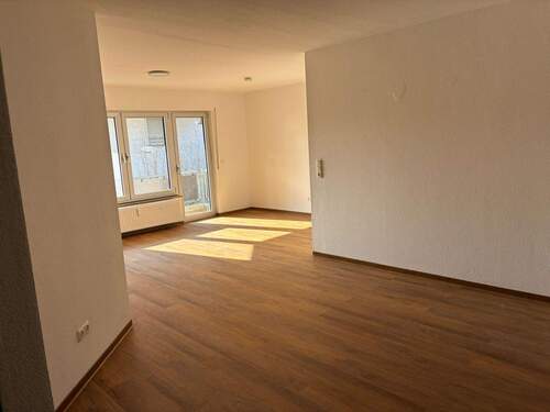 Blick in den Essbereich mit angrenzendem Wohnbereich und Zugang zum Balkon. Weiß angelegte Wände und brauner Vinyl-Designboden in Holzoptik. - 