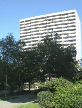 Außenansicht eines 19.stöckigen Mehrfamilienhauses umgeben von Bäumen und Sträuchern. - 