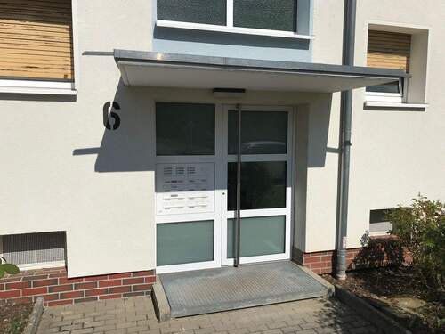 Hauseingang des mehrstöckigen Wohnhauses umgeben von Grünanlagen mit Bäumen - 