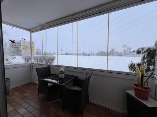 Gemütlicher Wintergarten mit Panoramablick auf verschneite Landschaft - 