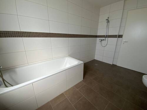 Blick in Bad mit weißen Wandfliesen, braunen Bodenfliesen Hänge-WC und bodengleiche Dusche - 