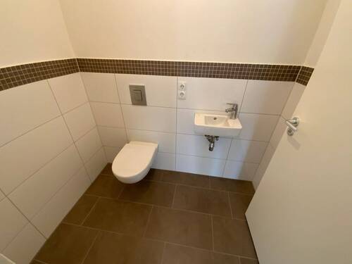 Blick in Gäste -WC mit weißen Wandfliesen, braunen Bodenfliesen Hänge-WC - 