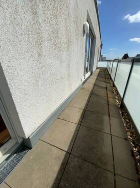 Blick vom Wohnraum auf den Balkon mit Glasbalkonbrüstung mit Trennwand aus Glas und grauem Boden und Rasenbereich - 