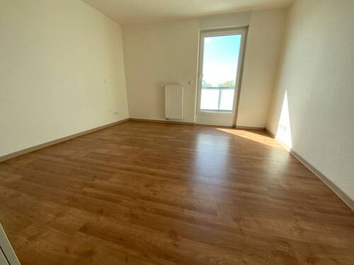 Blick von Diele in Schlafraum mit braunem PVC-Boden und weißen Wänden mit weißer ebenerdiger Balkontür - 