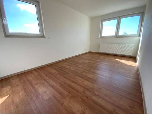  Blick von Diele in Schlafraum mit braunem PVC-Boden und weißen Wänden mit weißen ebenerdigen Fenstern - 