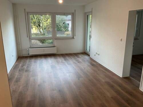 Wohnzimmer mit neuem Fußbodenbelag in Holzoptik, Wände tapeziert und weiß angelegt - 