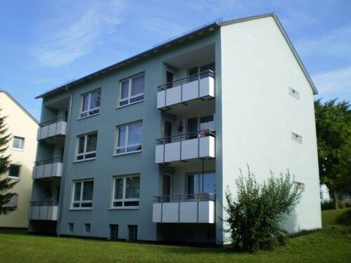 Rückansicht eines alleinstehenden 6-Parteienhauses mit Balkonen in grüner Umgebung - Ihr neues Zuhause: Freundliche 3-Zimmer-Wohnung mit Balkon in Korbach