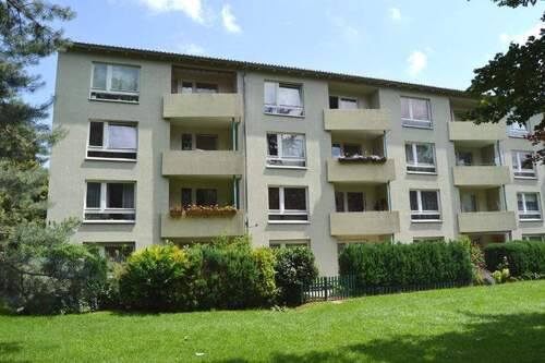 Rückansicht eines mehrstöckigen Wohngebäudes mit Balkonen, umgeben von Bäumen und grünen Sträuchern - Schicke 3-Zimmer-Wohnung - 510,00 EUR Kaltmiete, ca.  63,60 m² Wohnfläche