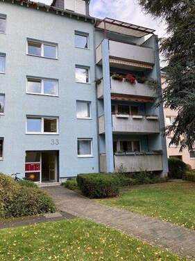 Eingangsbereich des mehrstöckigen Wohngebäudes umgeben von Grünanlagen mit Bäumen - 