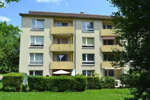 Rückansicht eines mehrstöckigen Wohngebäudes mit Balkonen, umgeben von Bäumen und grünen Sträuchern - Schicke 3-Zimmer-Wohnung - 532,00 EUR Kaltmiete, ca.  68,60 m² Wohnfläche