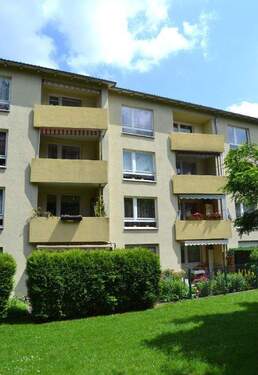 Rückansicht eines mehrstöckigen Wohngebäudes mit Balkonen, umgeben von Bäumen und grünen Sträuchern - 3 Zimmer Etagenwohnung zur Miete in Kassel