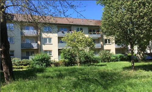Rückansicht eines mehrstöckigen Wohngebäudes mit Balkonen umgeben von grünen Sträuchern und Bäumen. - 2 Zimmer Etagenwohnung zur Miete in Frankfurt am Main