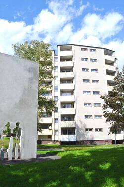 Rückansicht eines mehrstöckigen Wohngebäudes mit Balkonen, umgeben von Bäumen und grünen Sträuchern - 2 Zimmer Etagenwohnung zur Miete in Kassel