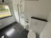 Blick in Bad mit weißen Wandfliesen, weißem Waschbecken, grauen Bodenfliesen, Hänge-WC und Dusch II.jpg - 
