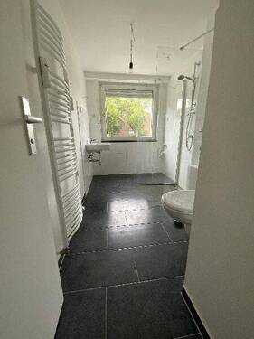 Blick in Bad mit weißen Wandfliesen, weißem Waschbecken, grauen Bodenfliesen, Hänge-WC und Dusche.jpg - 