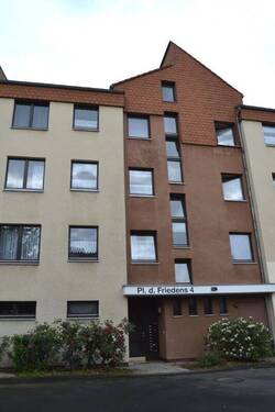 Platz des Friedens 4 - Blick auf den Eingangsbereich eines Gebäudes mit heller Fassade und dunkel akzentuierten Eingangsbereich - 1 Zimmer Etagenwohnung zur Miete in Baunatal