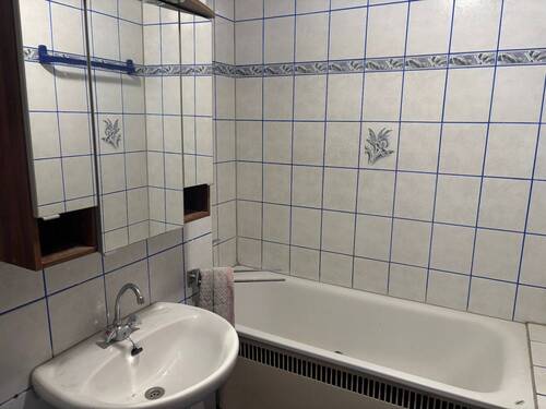 Das weiß geflieste Badezimmer verfügt über weiße Wandfliesen mit blauen Akzenten, einen Wandspiegel sowie eine Badewanne - Etagenwohnung mit 77,80 m&sup2; in Mannheim zur Miete