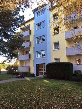 Gebäude Vorderseite des mehrstöckigen Wohnhauses umgeben von Grünanlagen mit Bäumen und Sträuchern - Für eine modernisierte Familienwohnung suchen wir neue Mieter!