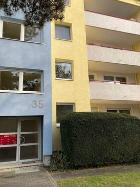 Eingangsbereich des mehrstöckigen Wohngebäudes umgeben von Grünanlagen mit Bäumen und Sträuchern - 