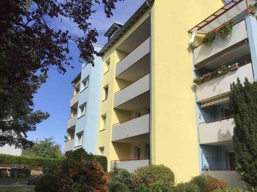 Rückansicht des mehrstöckigen Wohngebäudes mit Balkonen, umgeben von Grünanlagen mit Bäumen und grünen Sträuchern - 