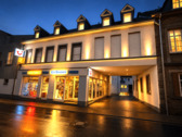 Abendliche Straßenszene mit Reisebüro.png - Frei ab sofort 2-Zimmer-Wohnung im 1. Obergeschoss Einbauküche Ohne Balkon Ohne PKW-Stellplatz